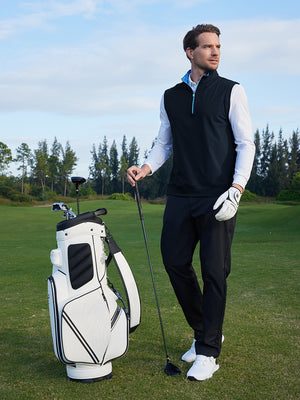 Model holding a golf club beside a golf bag on course, wearing print collar quarter zip golf vest in navy
