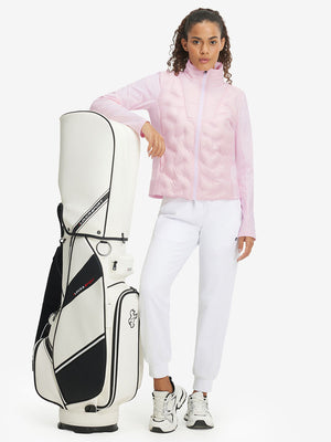 Model carrying a golf bag, wearing women's lightweight fleece-lined puffer jacket in light pink.