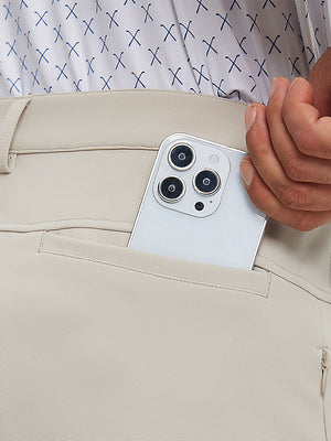 Close detail of hand placing phone into back pocket of lightweight moisture wicking dress pants in light khaki.