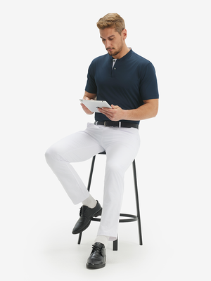 Full-body front: model in navy moisture-wicking short sleeve henley shirt on stool with iPad.